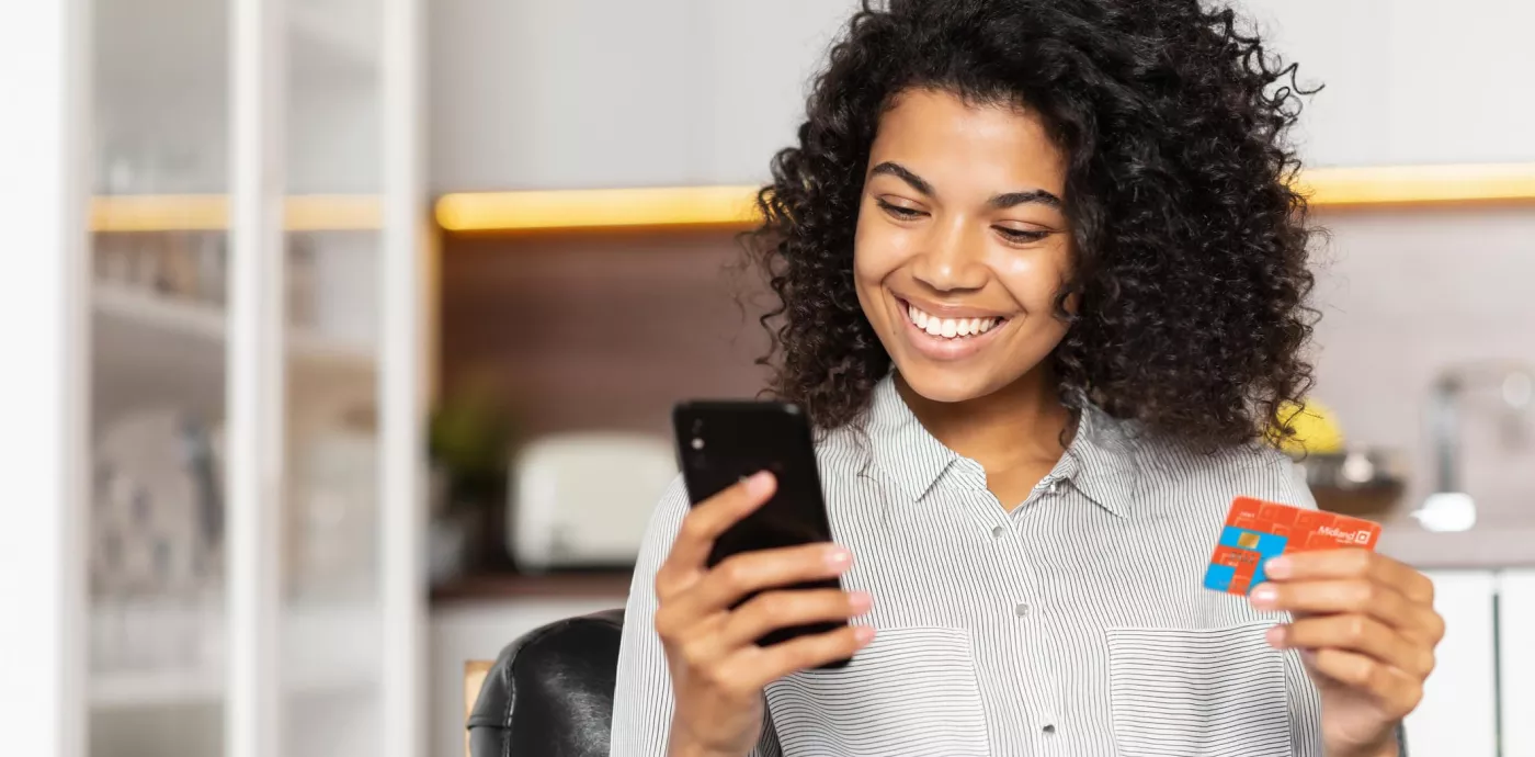 woman smiling while she holds Midland card and looks at phone